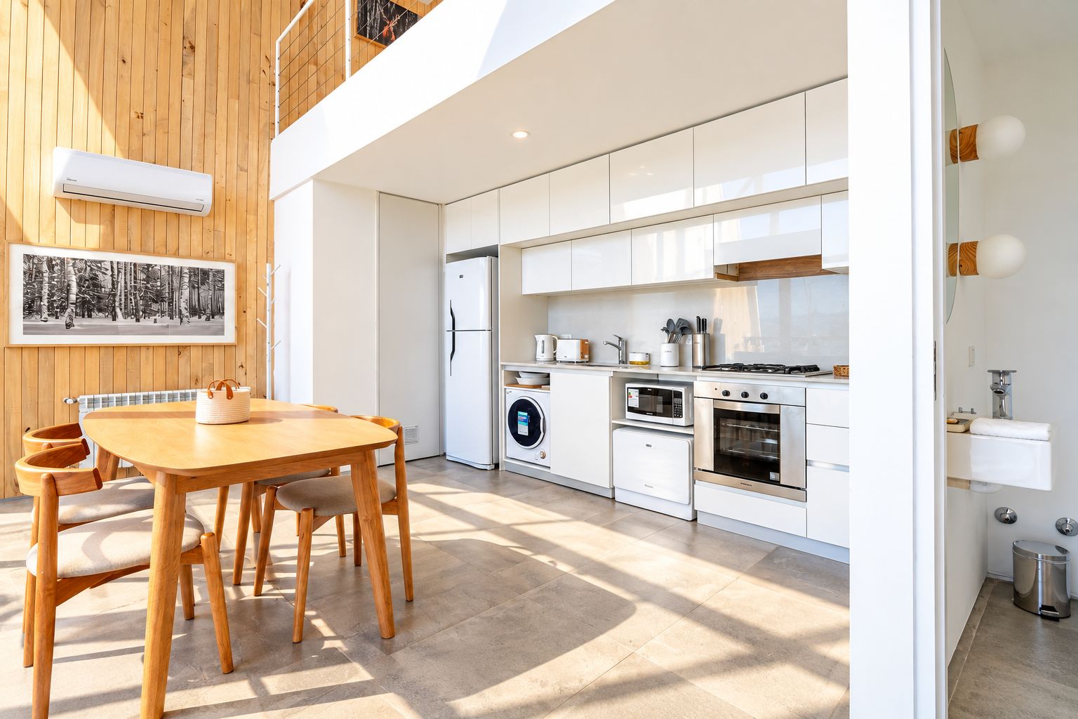 Una cucina moderna con mobili bianchi, un'area pranzo con tavolo e sedie in legno e un'ampia finestra che fa entrare luce naturale.