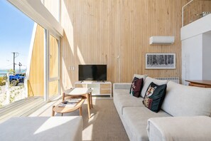 Ein modernes Wohnzimmer mit großem Fernseher, Holzwandverkleidung, einer Couch und einem Essbereich.