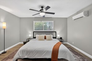 Ein Schlafzimmer mit einem Bett, einem Deckenventilator, einem Fenster mit Jalousien, einer Klimaanlage und Nachttischlampen.