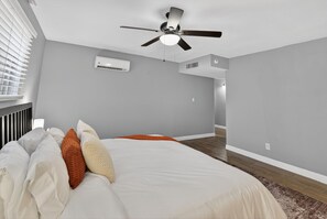 Een slaapkamer met een bed, een plafondventilator, een airconditioningssysteem en uitzicht op een andere kamer.