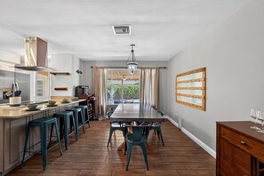 Een moderne keuken met een centraal eiland, barkrukken, een eettafel en uitzicht door een raam.
