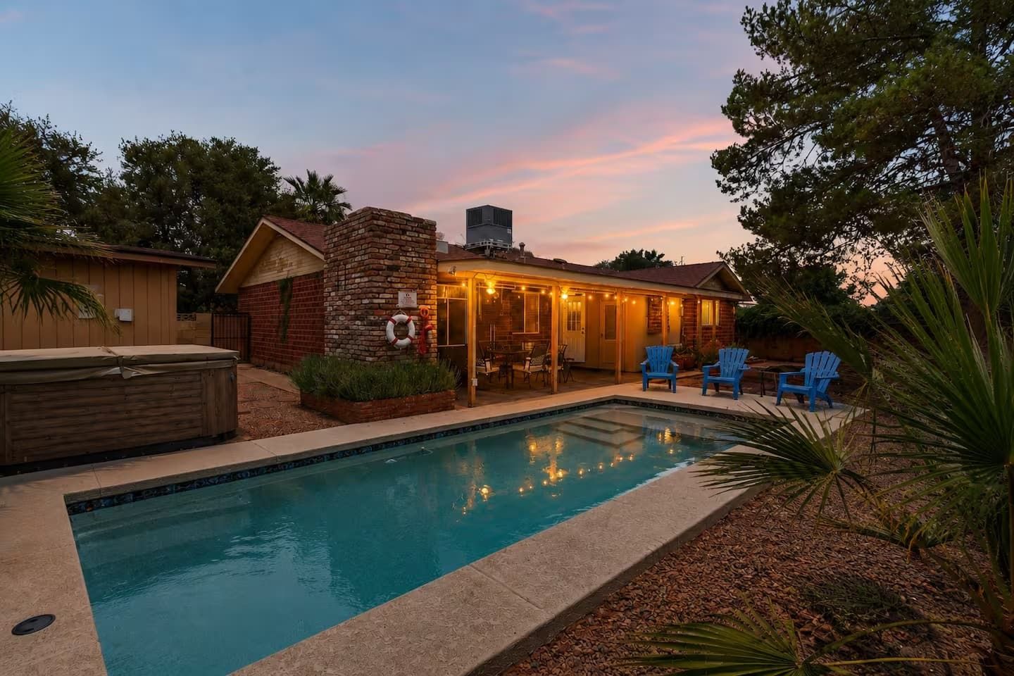 A backyard with a swimming pool, a covered patio area with string lights, and blue chairs.