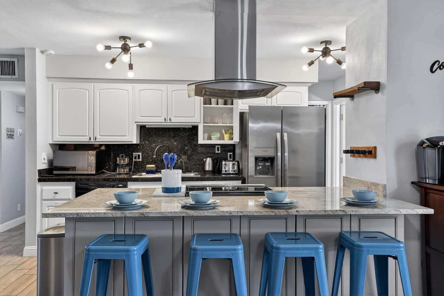 A modern kitchen with white cabinets, a central island with stools, stainless steel appliances, and pendant lighting.