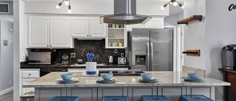 A modern kitchen with white cabinets, a central island with stools, stainless steel appliances, and pendant lighting.