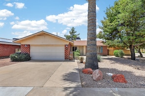 A residential property with a garage, a brick exterior, and a landscaped front yard with rocks and a palm tree. - Heated Pool & Hot Tub | Old Town | Sleeps 10+ (Scottsdale)