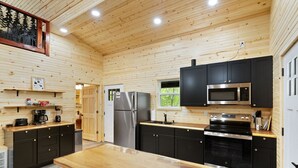 Cocina con paneles de madera, una isla central, armarios negros, electrodomésticos de acero inoxidable y un ventanal que proporciona luz natural.