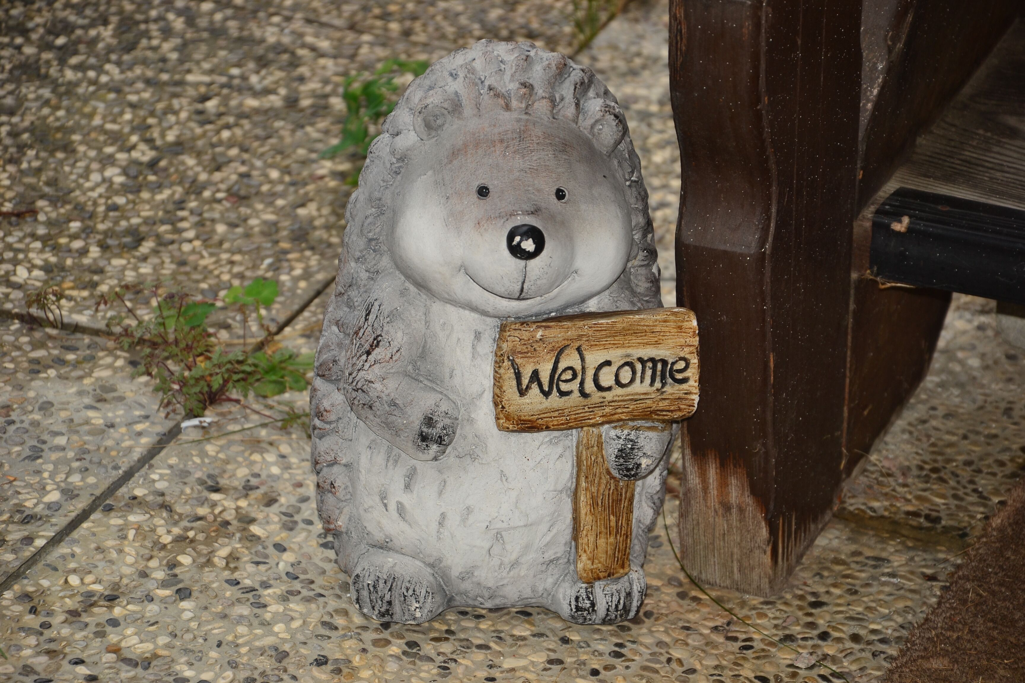A stone bear sculpture holding a wooden sign that says 'Welcome.'