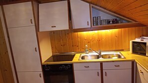 A compact kitchen with white cabinets, a black oven, a sink, and a microwave. - Eden Apartment (Glödnitz)