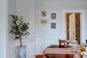 Een eethoek met een houten tafel gedekt voor vier personen, een vaas met groene bladeren en kunstwerken in lijsten aan de muur.
