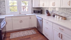 A kitchen with white cabinets, a microwave, and a sink. - The Magnolia | 1900 Historic•Grand Piano•3 KingBRs (Alachua)