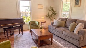 A living room with a piano, a green armchair, a grey sofa, a wooden coffee table, and a plant. - The Magnolia | 1900 Historic•Grand Piano•3 KingBRs (Alachua)