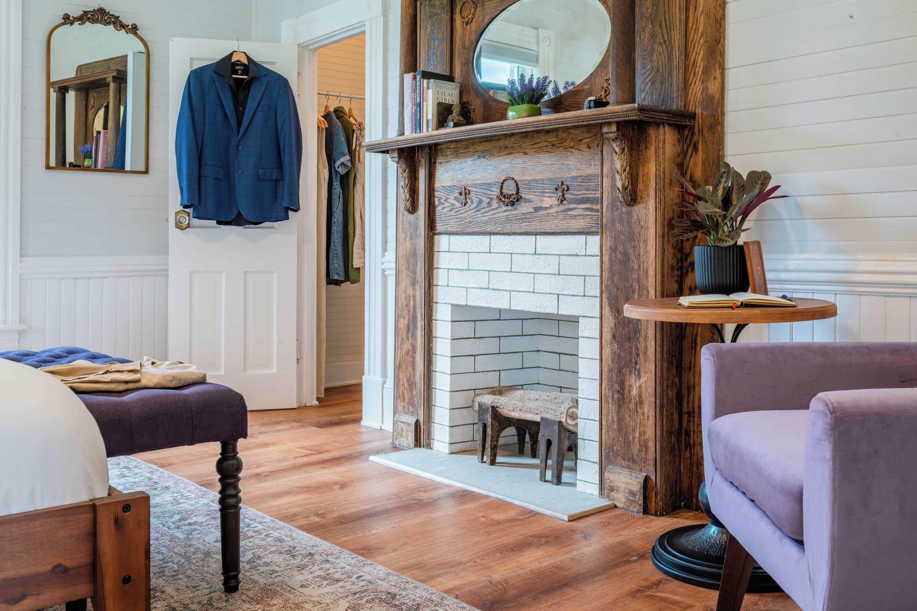 A room with a fireplace, a bed, a chair, and a coat rack with a blue jacket.