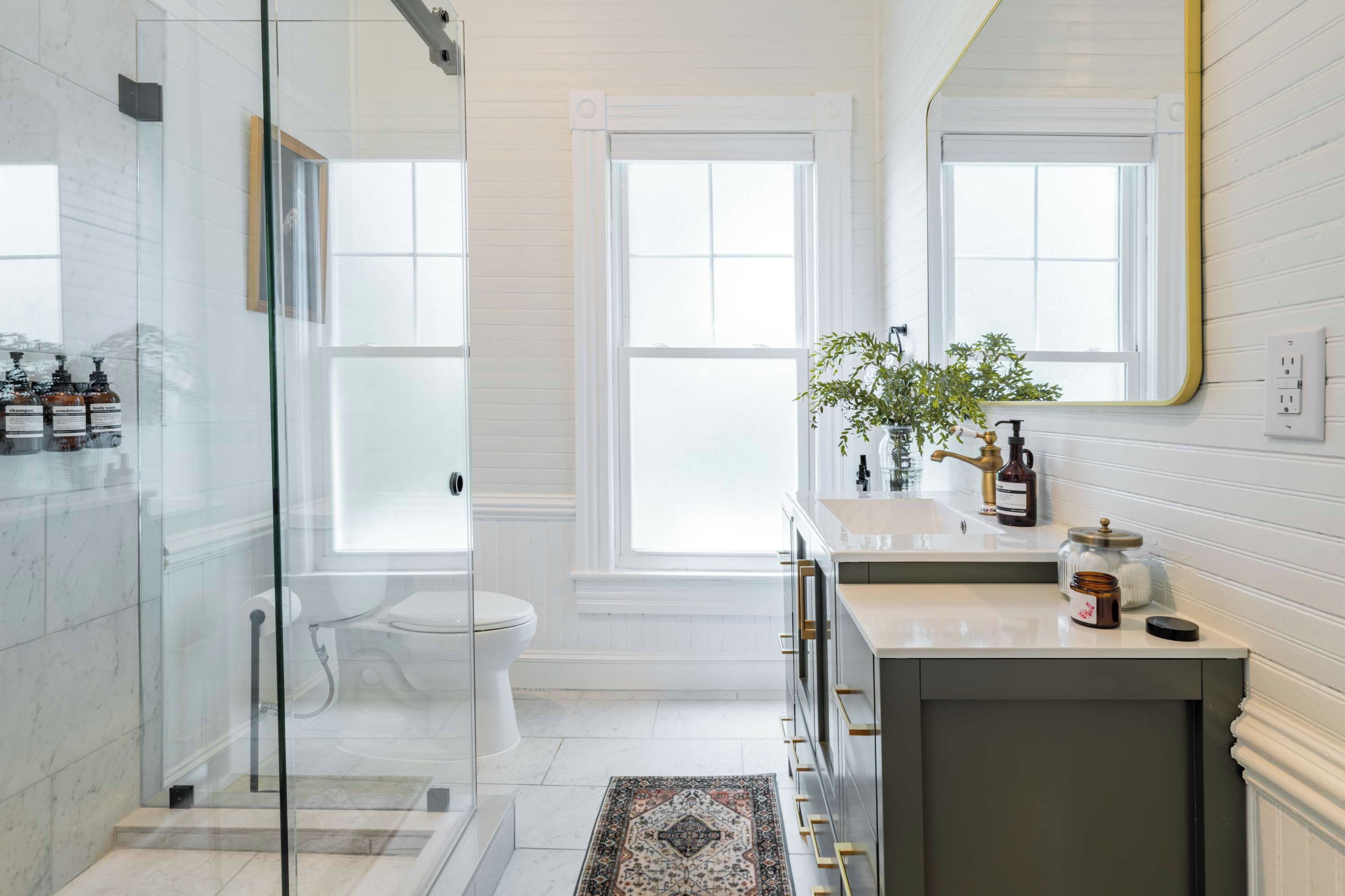 A modern bathroom with a glass shower enclosure, a toilet, a sink with a mirror, and a window providing natural light.