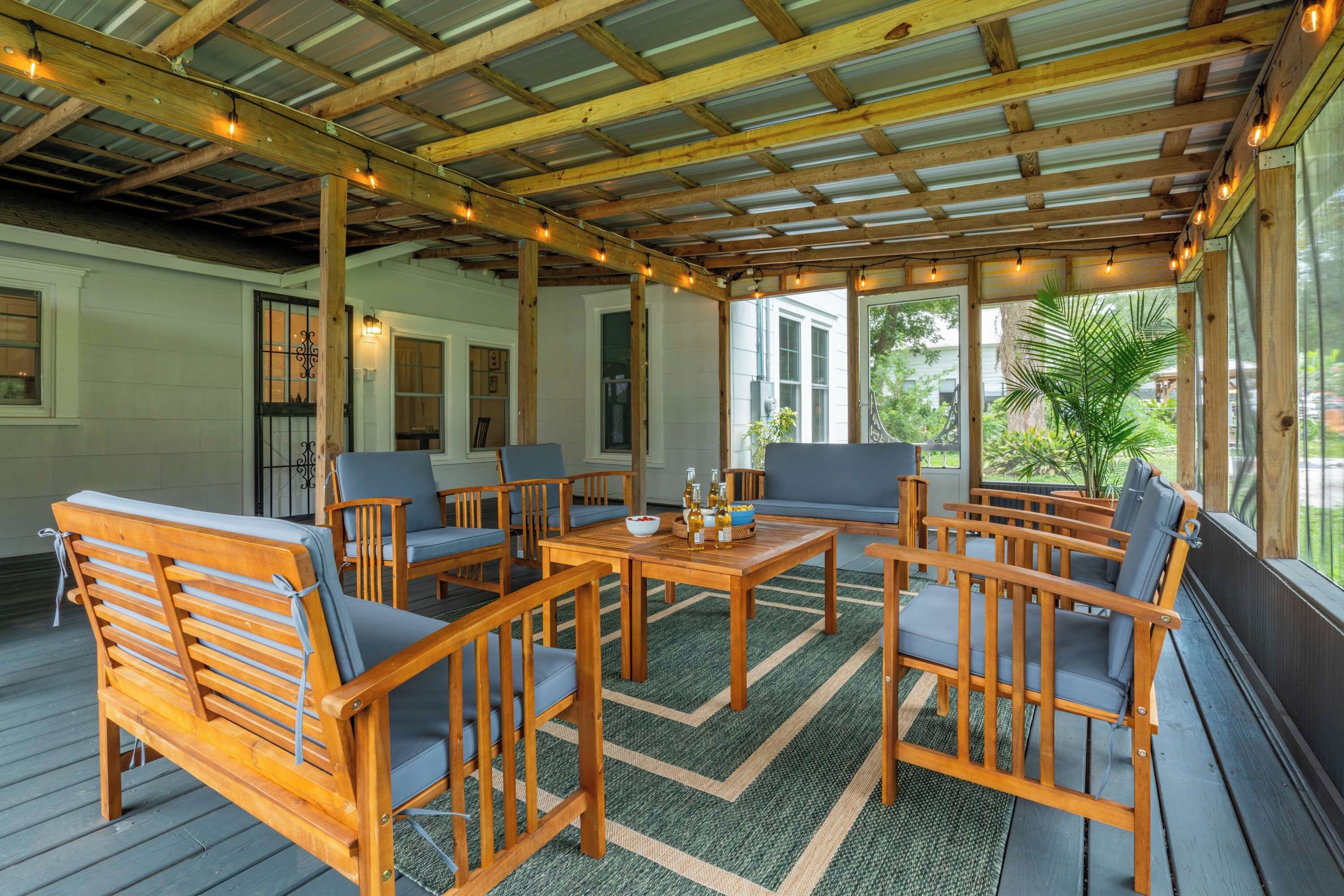 Un patio techado al aire libre con mobiliario de madera, una mesa y luces colgantes.