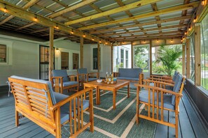Een overdekt terras buiten, met houten meubels, een tafel en lichtjes.