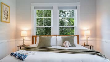 Ein Schlafzimmer mit einem großen Bett, zwei Nachttischlampen und einem Fenster mit Blick auf Grünflächen.