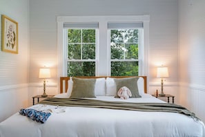 Een slaapkamer met een groot bed, twee bedlampen en een raam met uitzicht op groen.