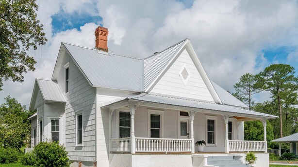 A white two-story house with a gabled roof, a front porch with white railings, and a brick chimney. - The Magnolia | 1900 Historic•Grand Piano•3 KingBRs (Alachua)