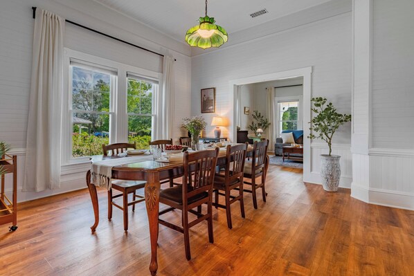 A dining area with a wooden table and chairs, large windows, and a hanging light fixture.