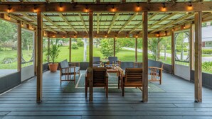 A covered outdoor seating area with wooden furniture and string lights. - The Magnolia | 1900 Historic•Grand Piano•3 KingBRs (Alachua)