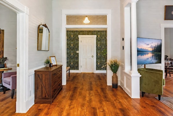 Een gang met een houten vloer, een spiegel, een dressoir, een bankje en een televisie.