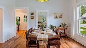 A dining room with a wooden table set for six, surrounded by chairs, with a green pendant light above. - The Magnolia | 1900 Historic•Grand Piano•3 KingBRs (Alachua)