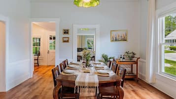 A dining room with a wooden table set for six, surrounded by chairs, with a green pendant light above.