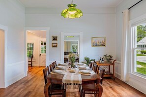 Een eetkamer met een houten tafel gedekt voor zes personen, omringd door stoelen, met een groene hanglamp erboven.