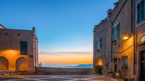 Un patio empedrado flanqueado por edificios, con puertas y ventanas de arco y contraventanas.