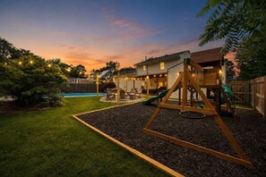 Ein Garten mit Schaukel, Pool und einem Haus im Hintergrund.