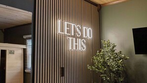 Ett rum med en vägg som består av träribbor, en neonskylt med texten ”LÅT OSS GÖRA DET HÄR” och en krukväxt.