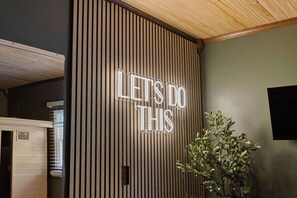 Ein Zimmer mit einer Wand aus Holzlamellen, einem Neonlichtschild mit der Aufschrift 'LET'S DO THIS' und einem Blumentopf.
