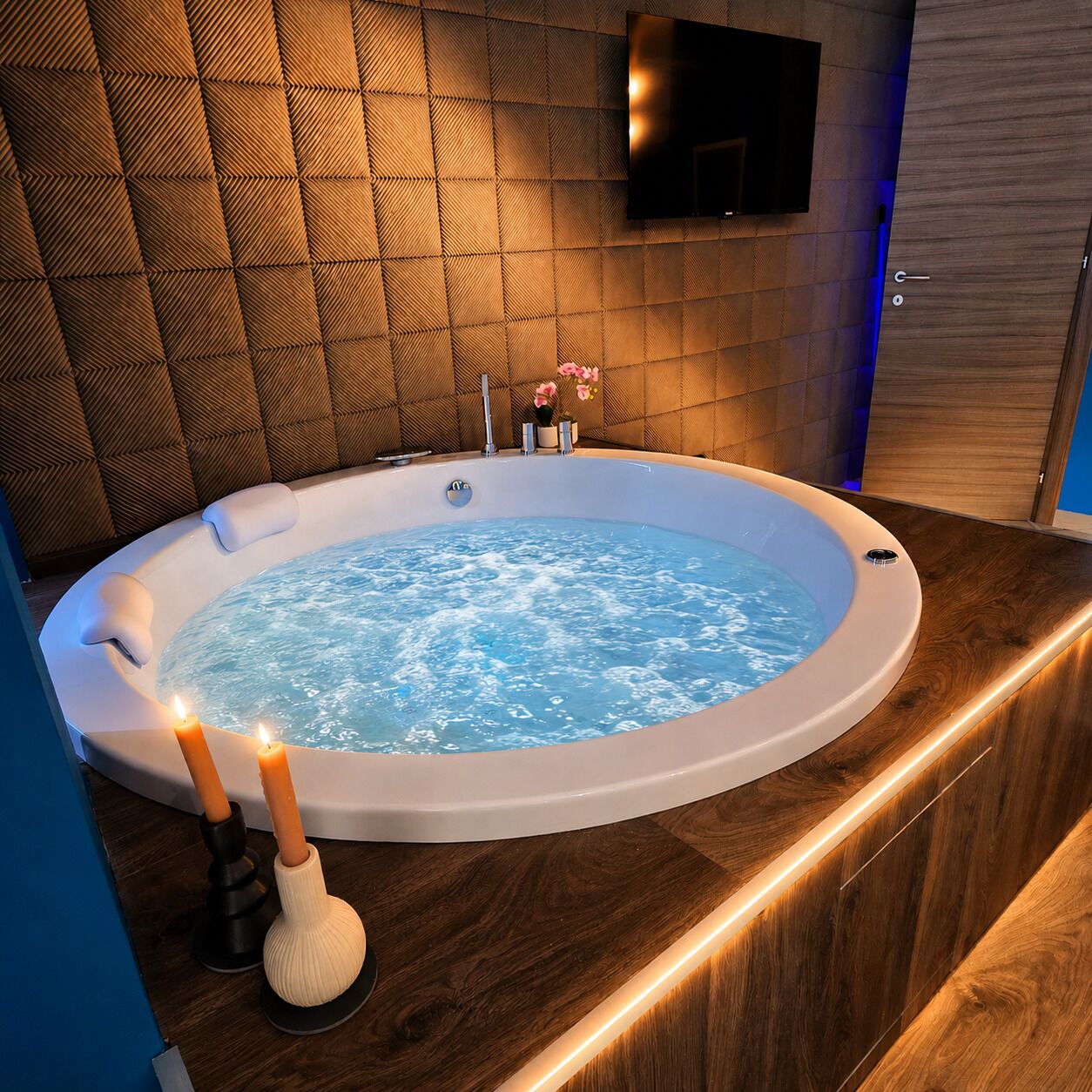 Ein modernes Badezimmer mit Whirlpool, Holzboden, Wand-Fernseher und Kerzen.
