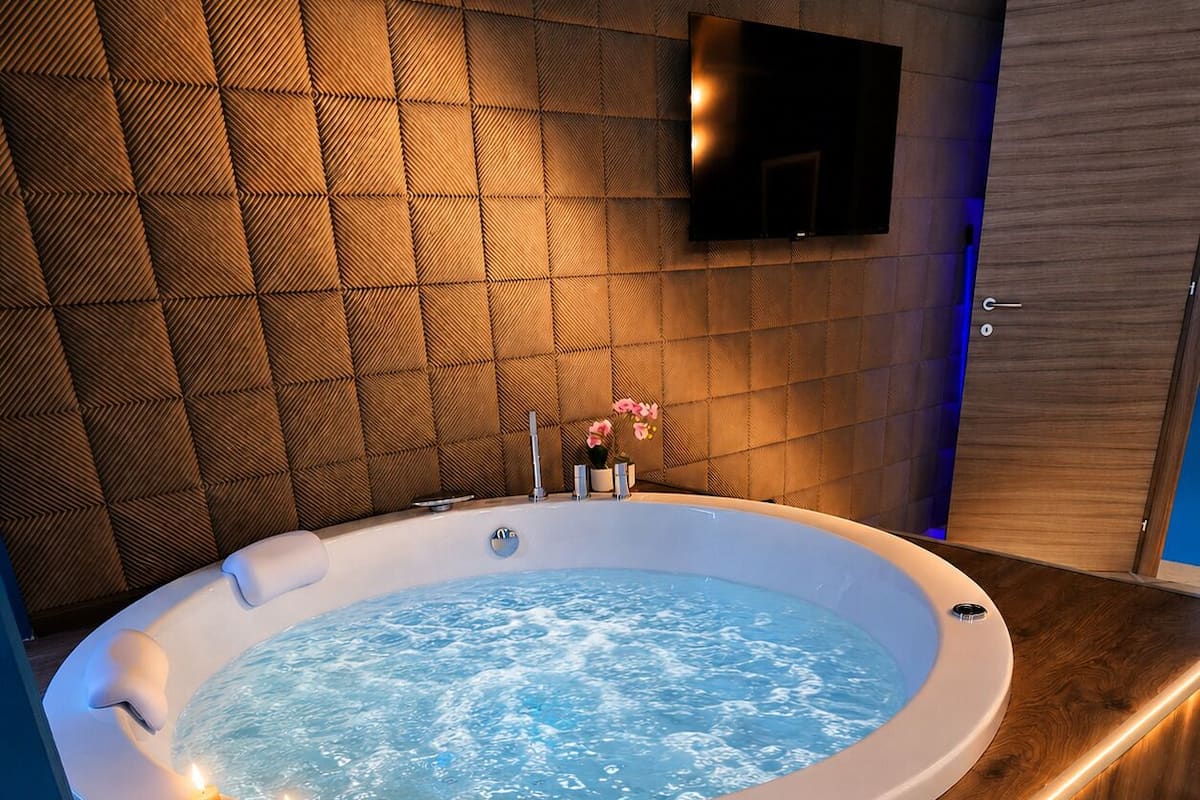 Une salle de bain moderne avec un jacuzzi, un plancher en bois, un téléviseur fixé au mur et des bougies.