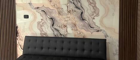 A room with a black sofa, a wooden coffee table, and a marble-patterned wall.