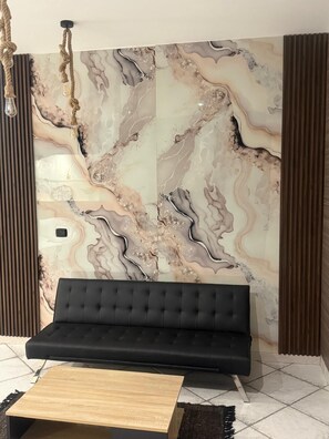 Ein Zimmer mit einem schwarzen Sofa, einem Holztisch und einer Wand mit Marmormuster.