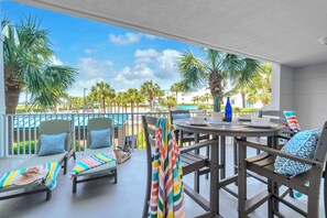 Ein Balkon mit Liegestühlen, einem Esstisch und Blick auf einen Pool und Palmen.