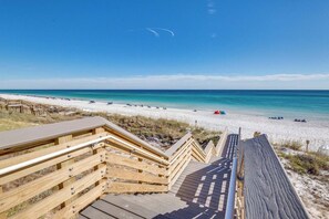 Ein hölzerner Steg führt zu einem Strand bei strahlendem Himmel.