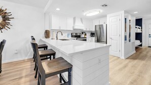 Une cuisine moderne avec des meubles blancs, un grand îlot central et un coin repas doté de chaises en bois.