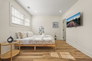 Un dormitorio con cama, televisión, ventana y un cuadro en la pared.