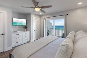 Ein Schlafzimmer mit einem Bett, Deckenventilator, Fernseher, einer Schiebetür zum Balkon und Blick aufs Meer.