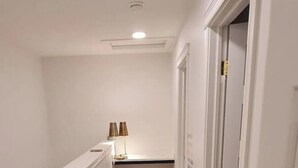 En smal hall med ett mattbeklätt golv, vita väggar och en taklampa.