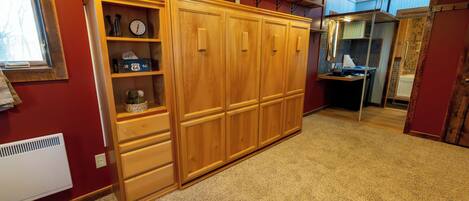 A room with a wooden wardrobe, a radiator, and a mirror reflecting a bathroom.