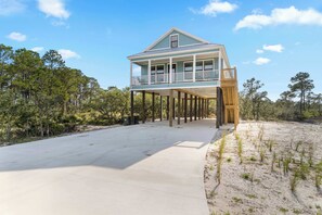 A two-story house with a balcony, a concrete driveway, and surrounding trees. - Newly Built Gulf Shores Getaway with Gas Grill (Gulf Shores)