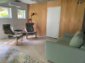 A room with a green sofa, two armchairs, a patterned rug, wooden walls, and a white door. - Spacious Apartment near Enschede City Centre (Enschede)