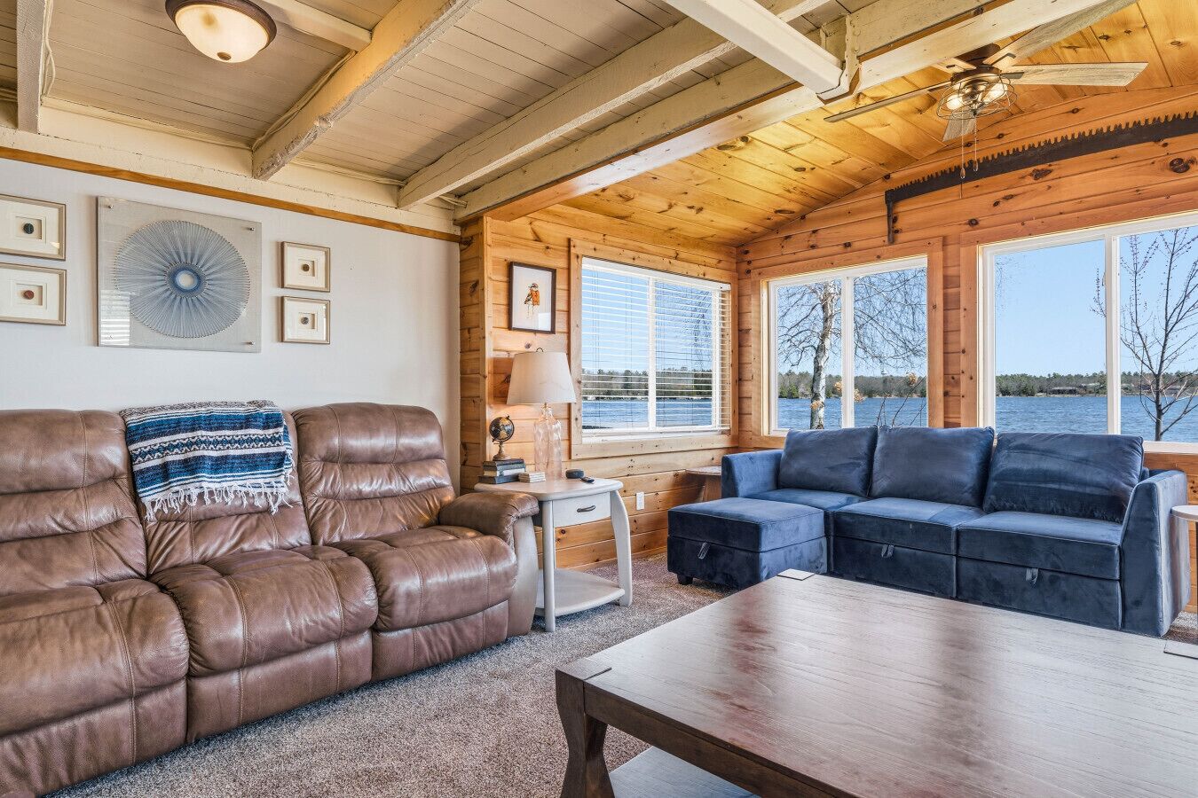 L’intérieur d’un chalet chaleureux, avec un canapé en cuir, un divan bleu et une table en bois.