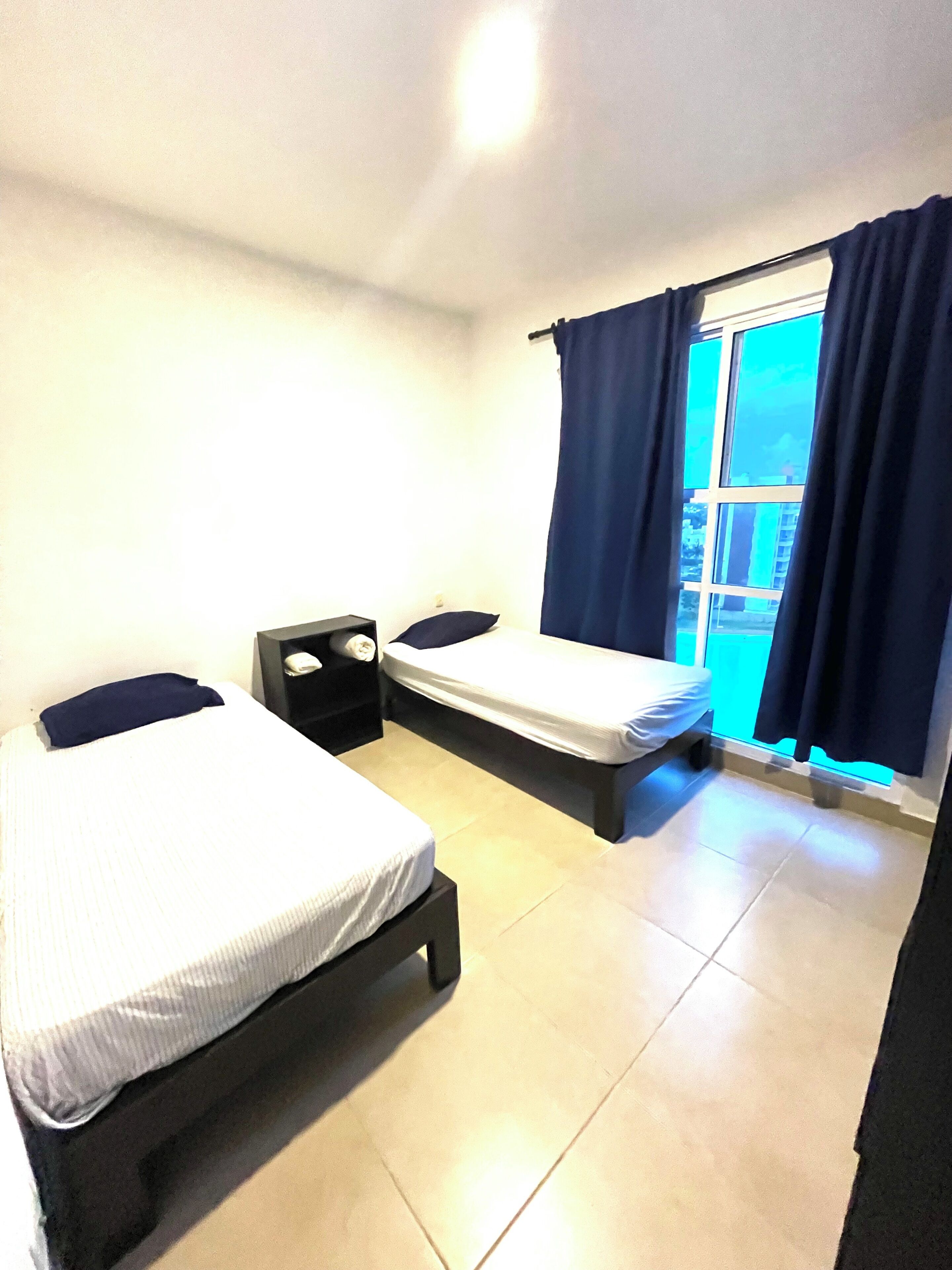 Een kamer met twee bedden, een tafeltje en een raam met gordijnen.