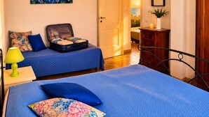 Een slaapkamer met een bed, een koffer, een lamp, een dressoir en een schilderij aan de muur.
