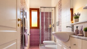 Een badkamer met douche, toilet en wastafel, met een roze kleed en een plant in pot.