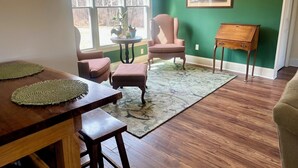 Una habitación con una mesa de madera, dos sillas, una mesita auxiliar, una alfombra y un cuadro en la pared.